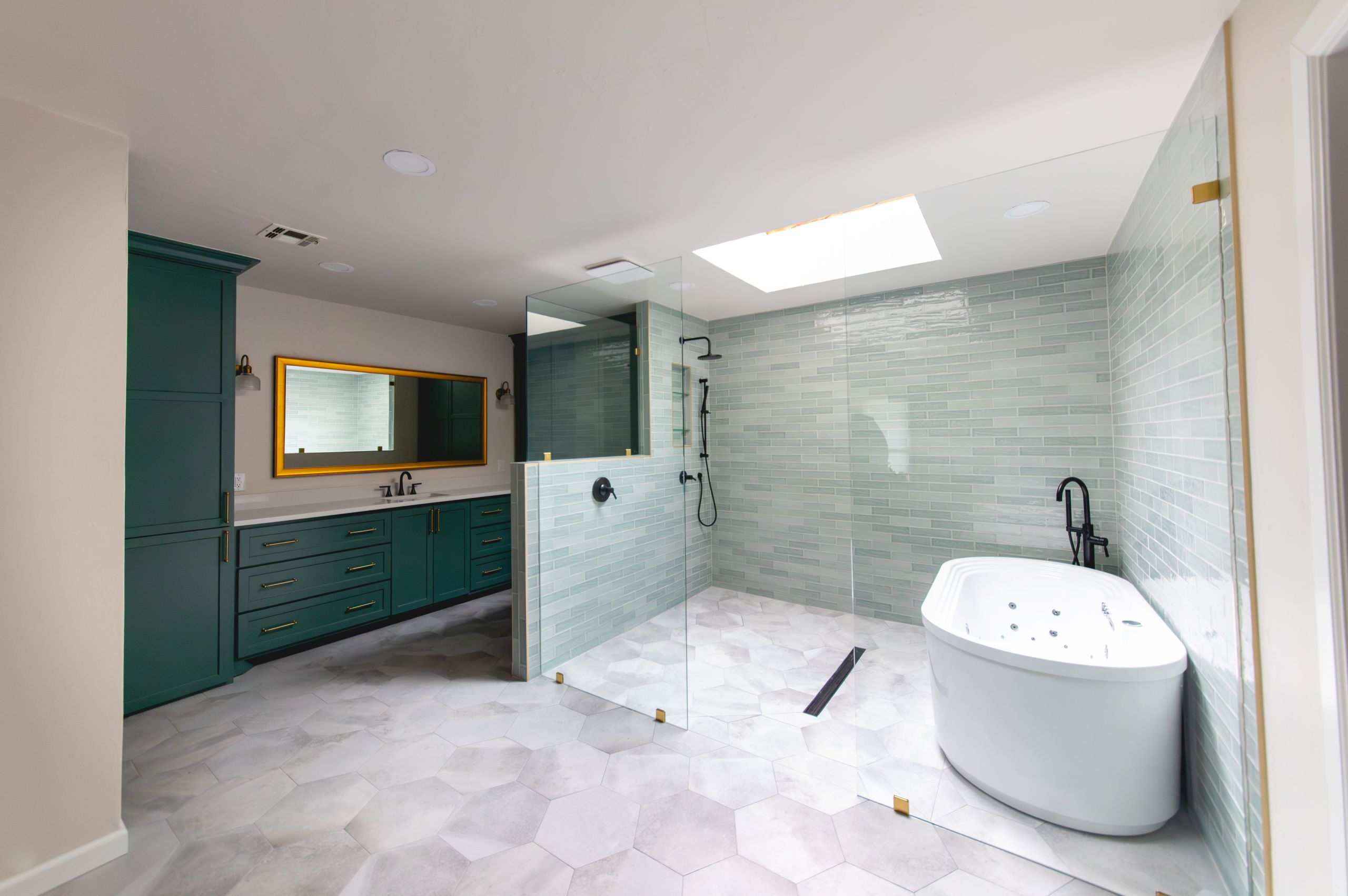Spacious bathroom with green cabinets, walk-in glass shower, and a white soaking tub beneath a skylight.