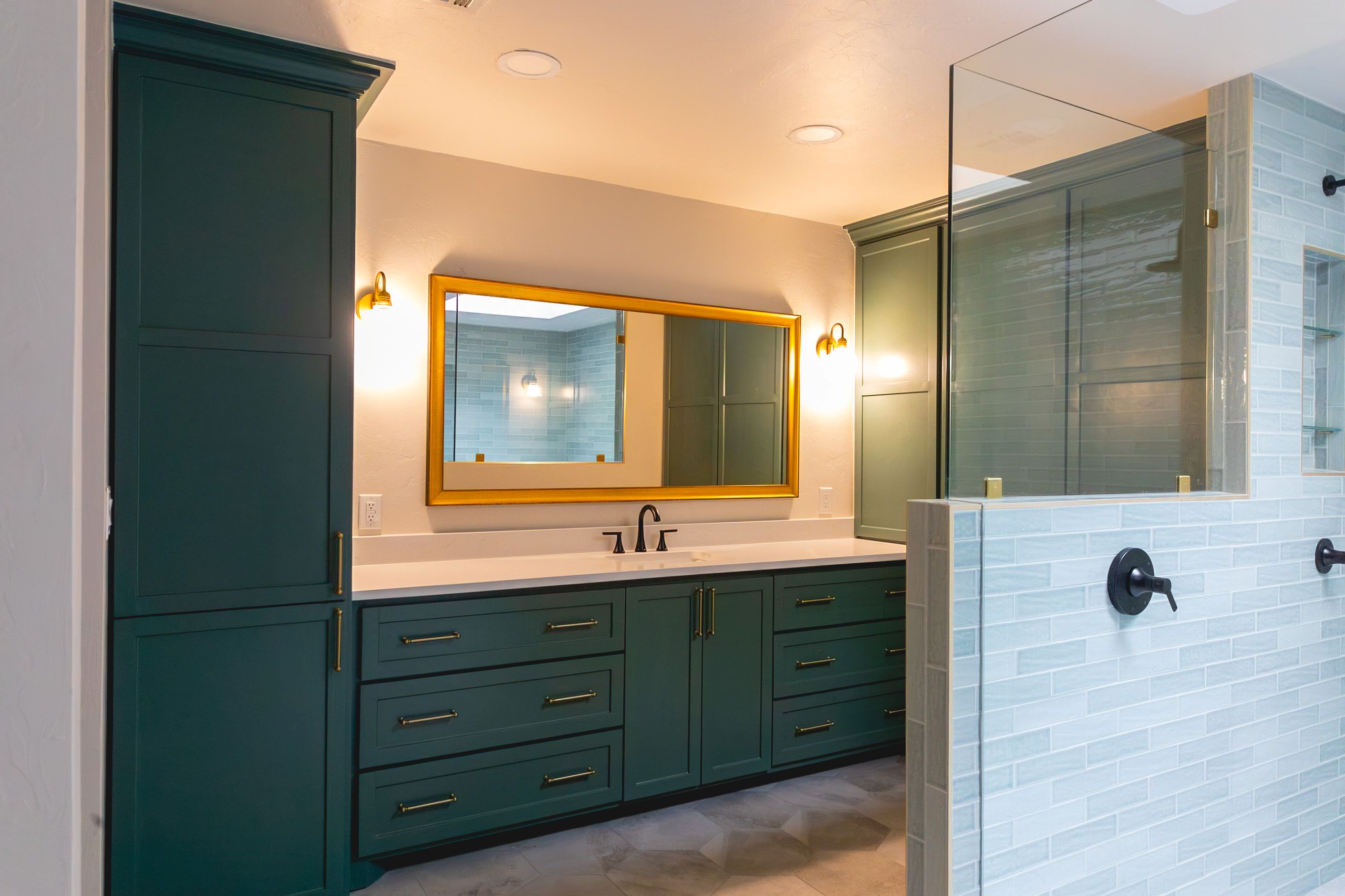 Double-sink vanity with green cabinetry, a large gold-framed mirror, and warm wall sconces.