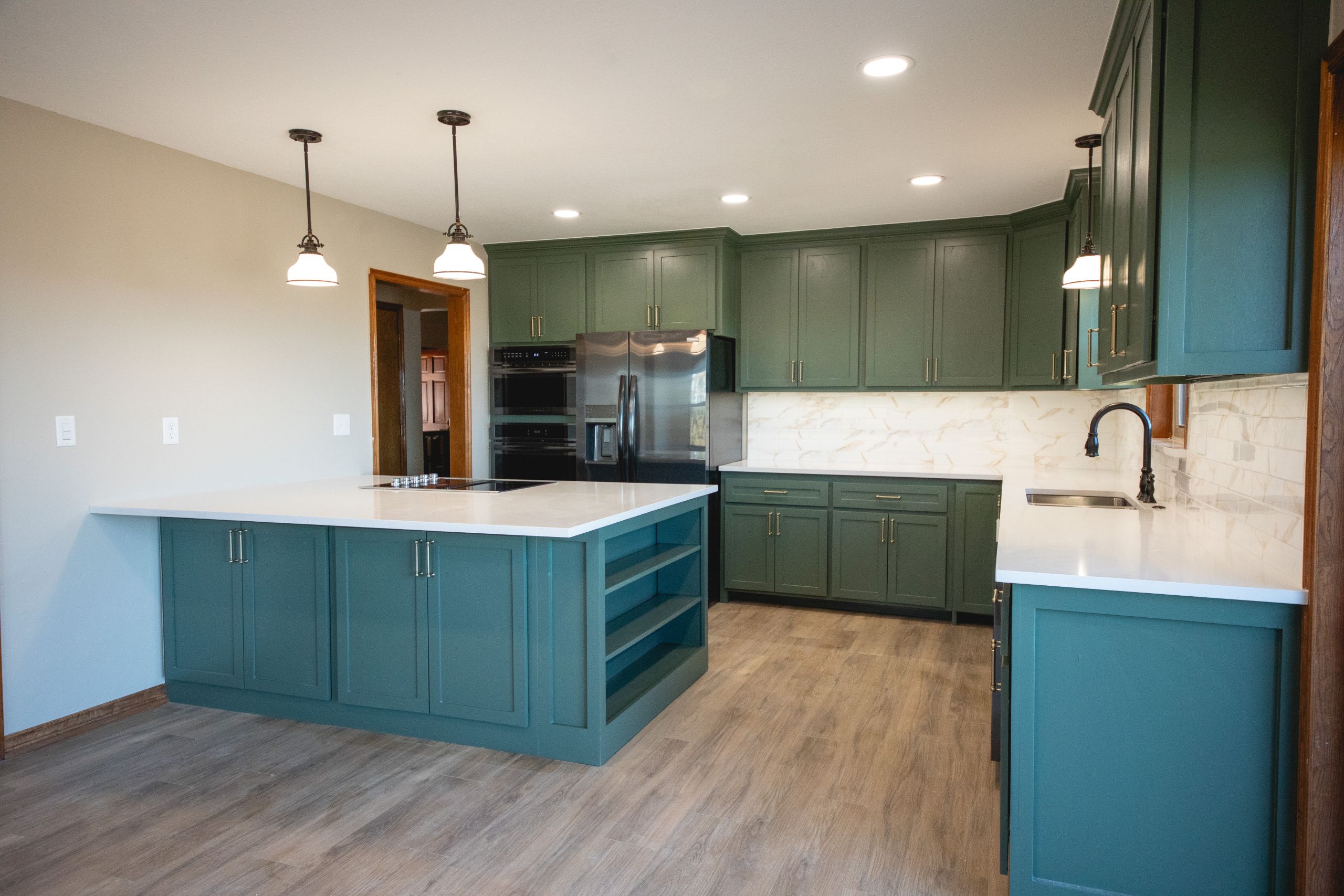 Modern kitchen with green cabinets, stainless steel appliances, and a white quartz island.