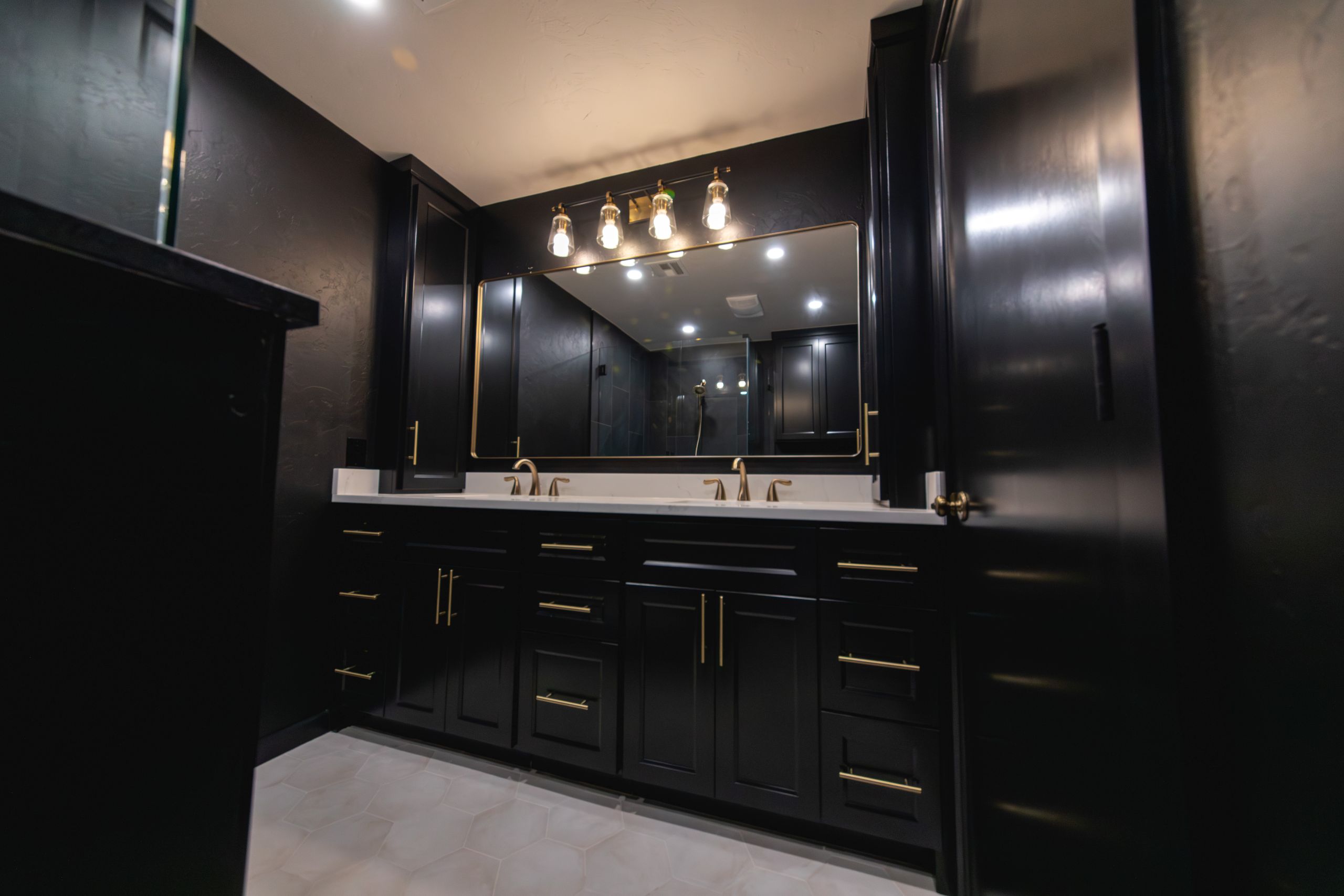 Wide view of double-sink black vanity with gold hardware and large mirror.