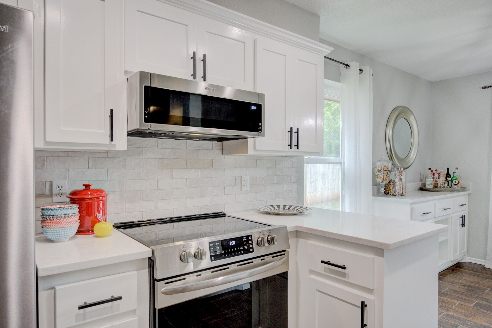 White kitchen featuring stainless steel stove, microwave, and pops of red and yellow countertop decor.