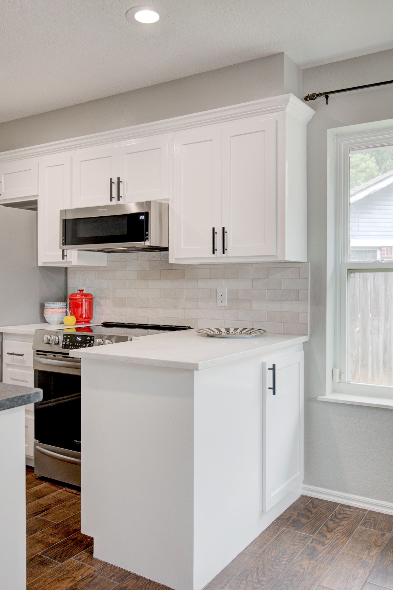 Bright kitchen corner with white cabinets, stainless steel appliances, and subway tile backsplash.