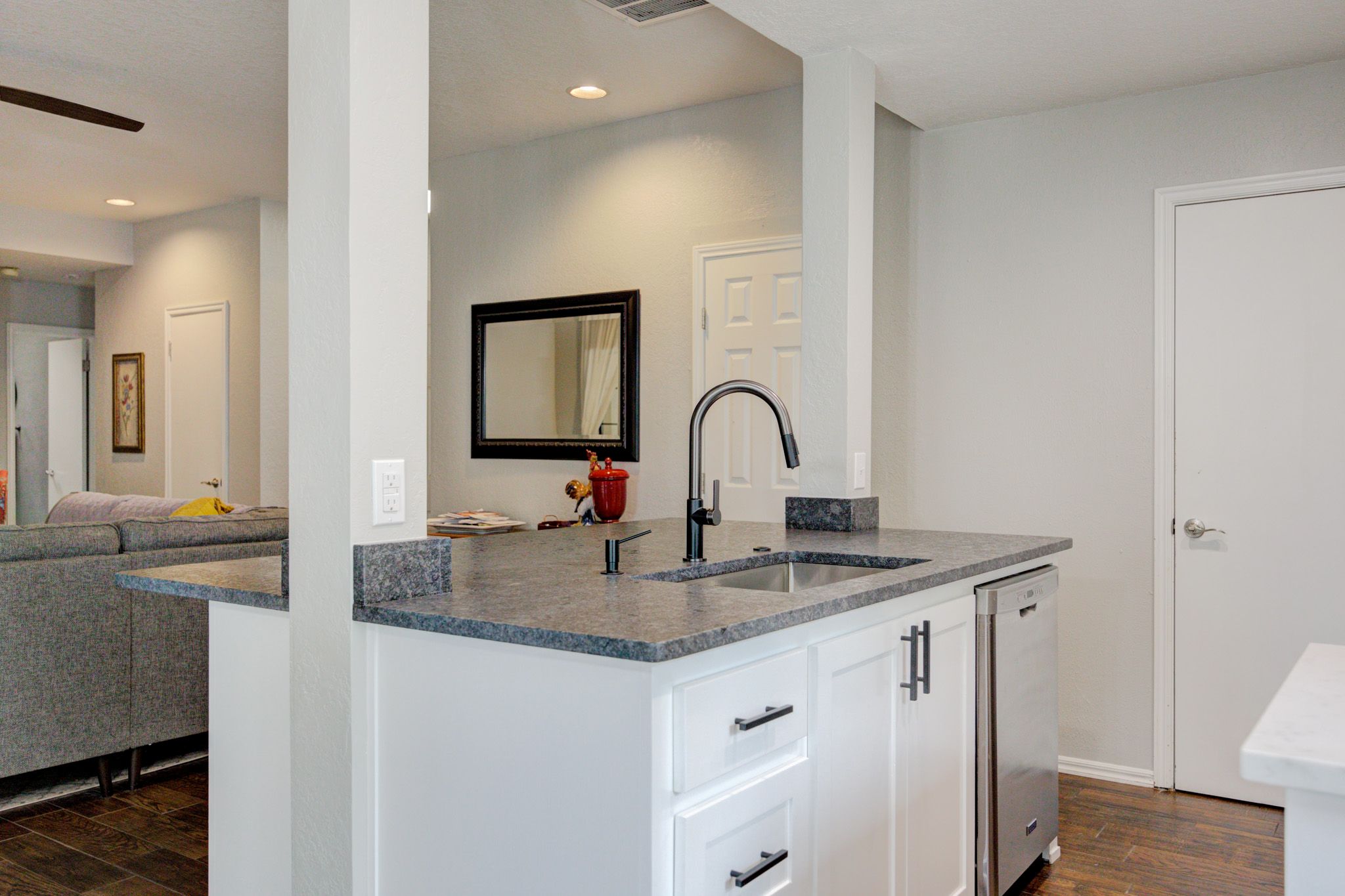 Kitchen island with black faucet, white cabinetry, and view into a neutral-toned living room.