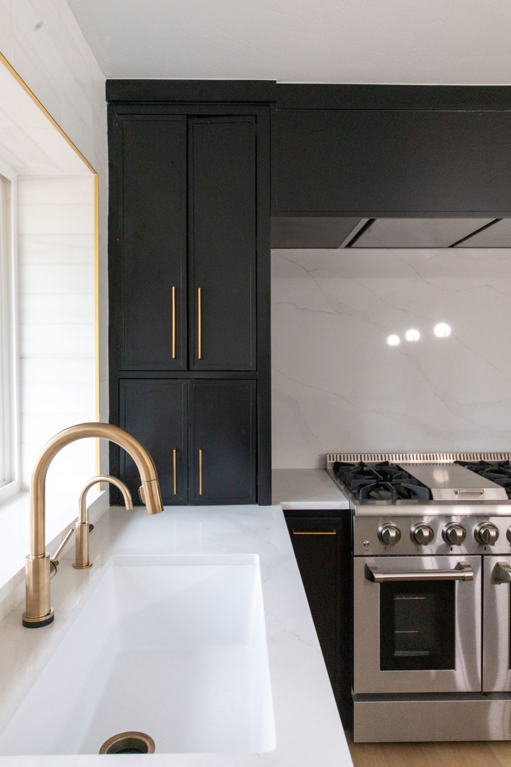 Kitchen detail with brass faucet, white sink, and black cabinetry with gas cooktop