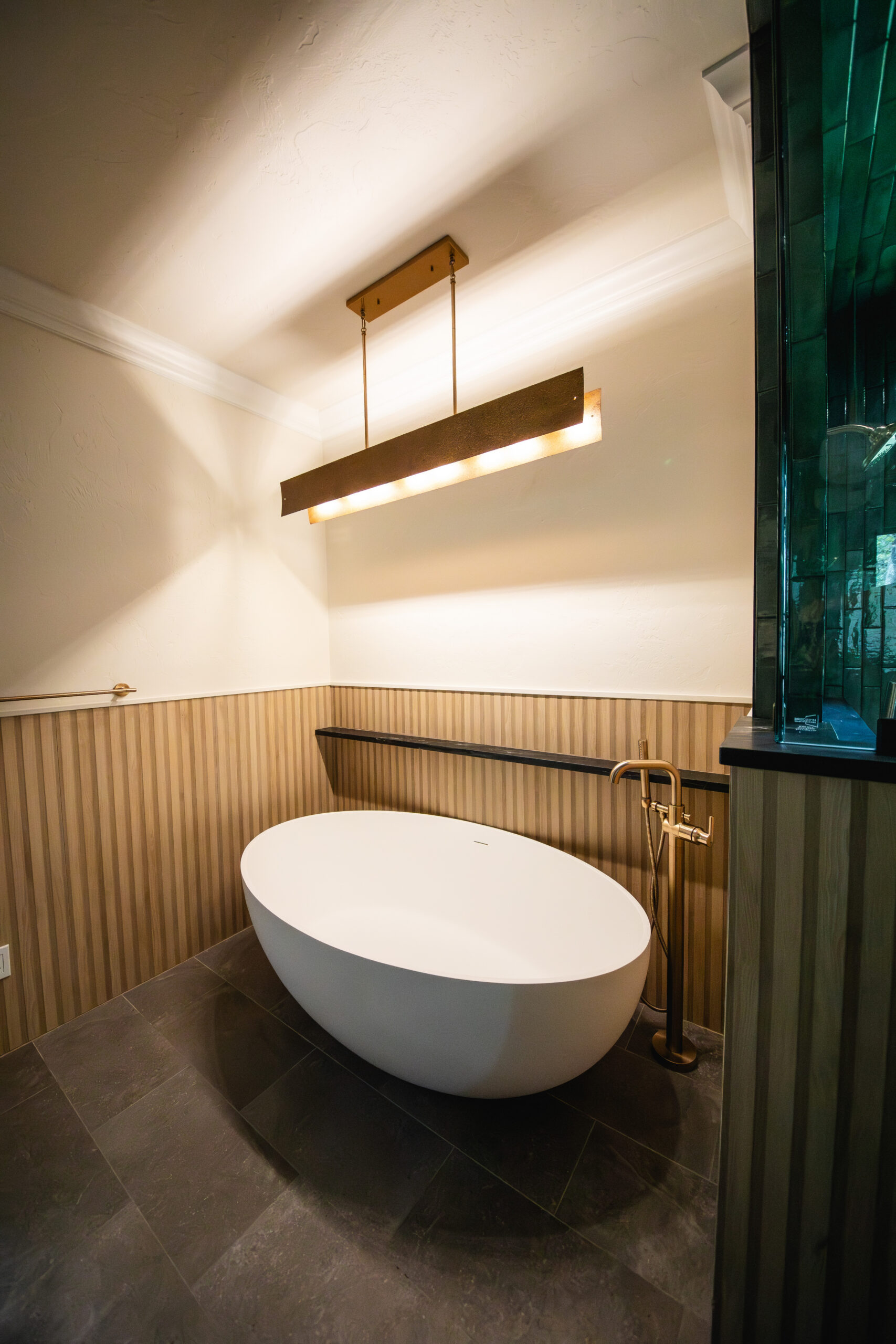 Modern bathroom with freestanding tub, wood paneling and green tile accents.