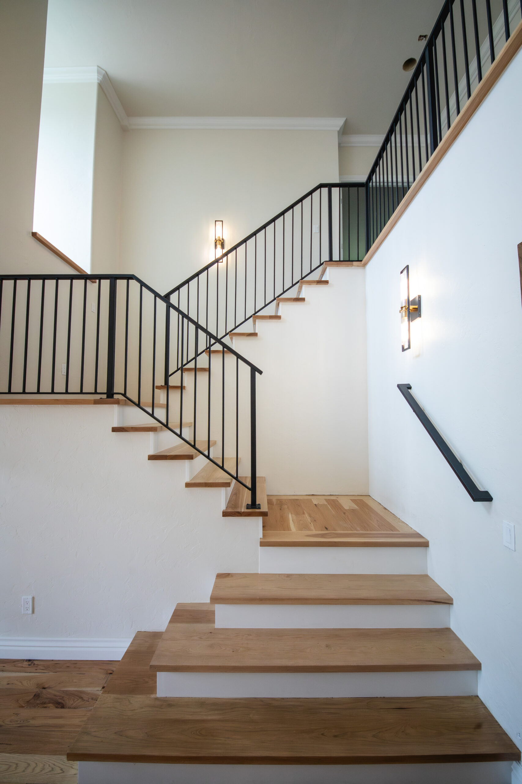 Modern wood staircase with black metal railings and white walls in a bright open interior.