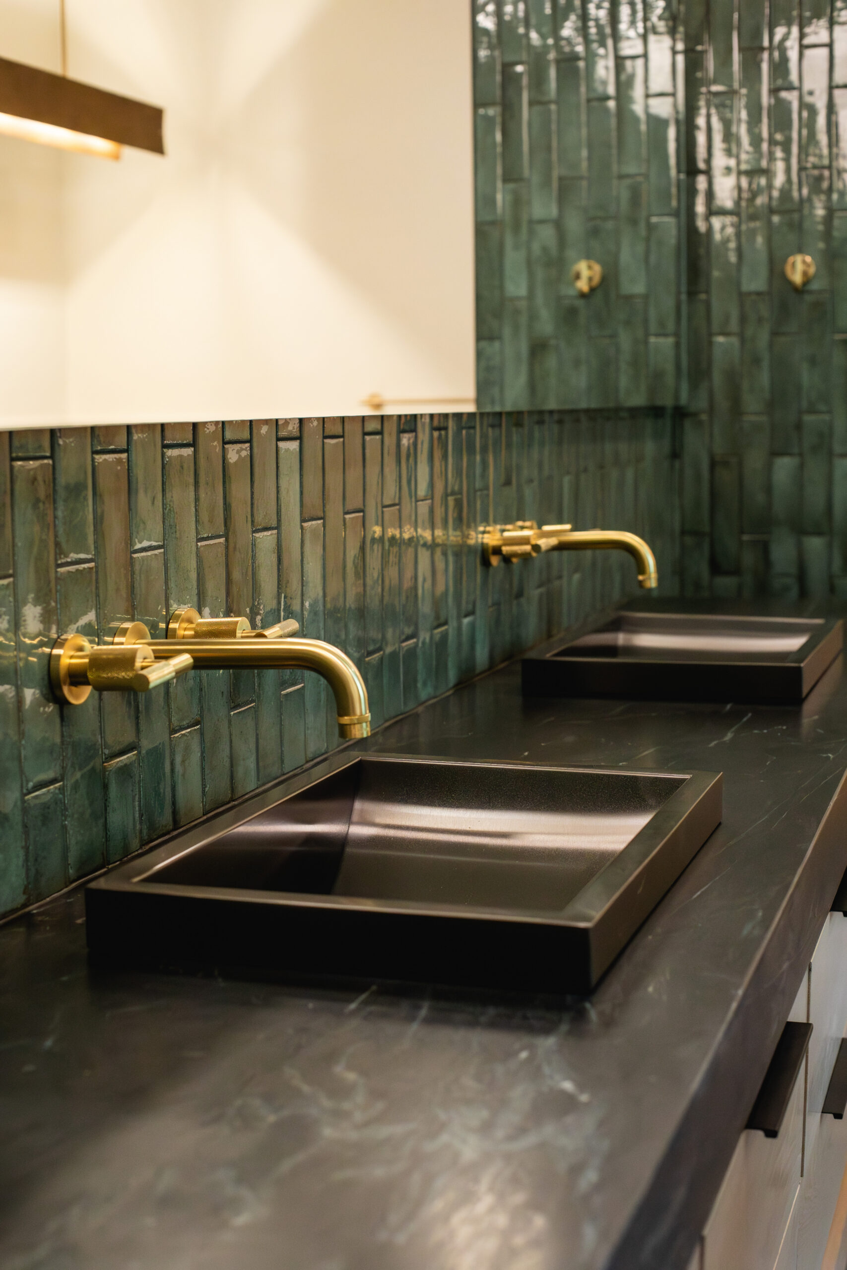 Black rectangular sinks with brass wall-mounted faucets and green tile backsplash.