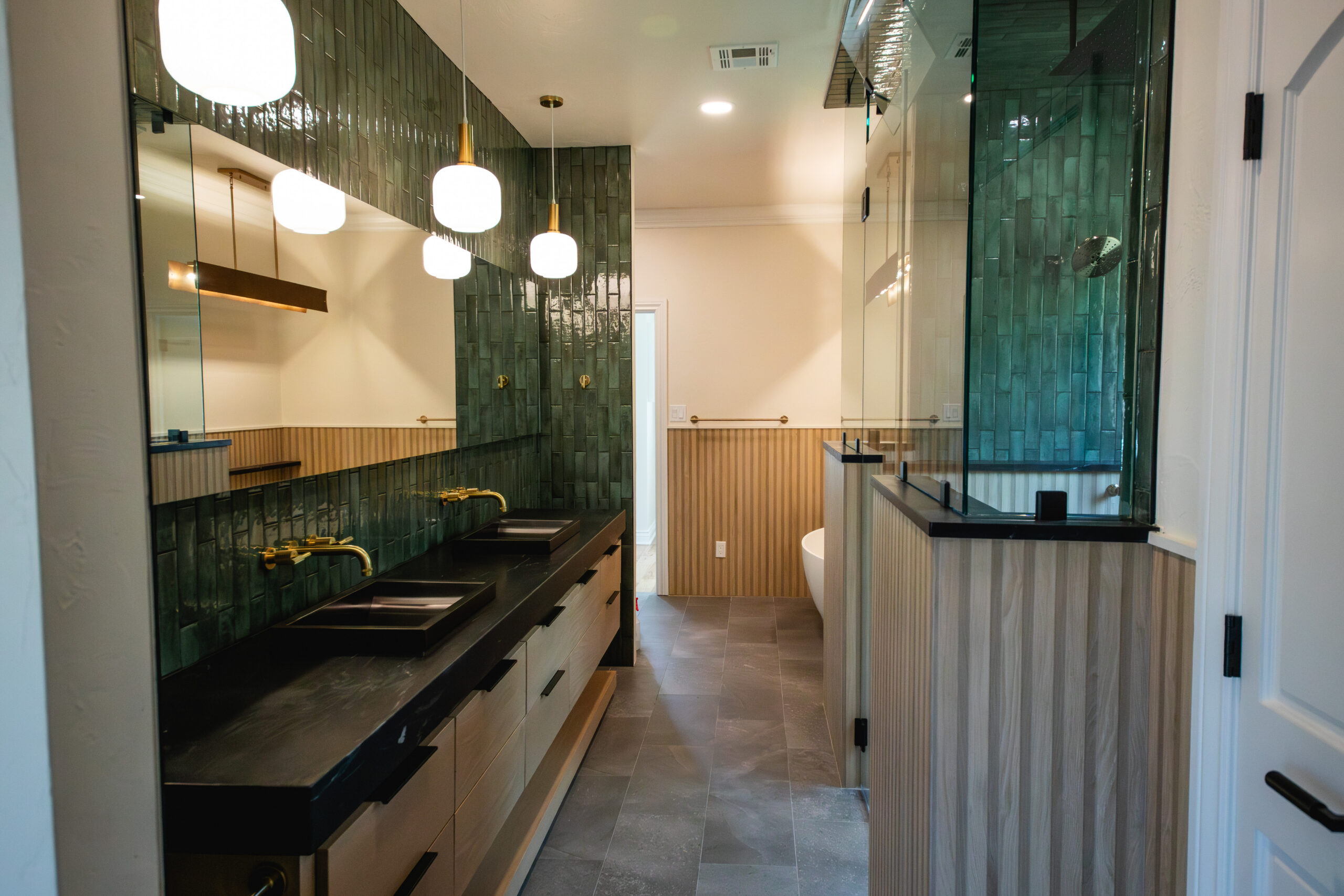 Modern bathroom with double vanity, green tile walls and glass shower enclosure.
