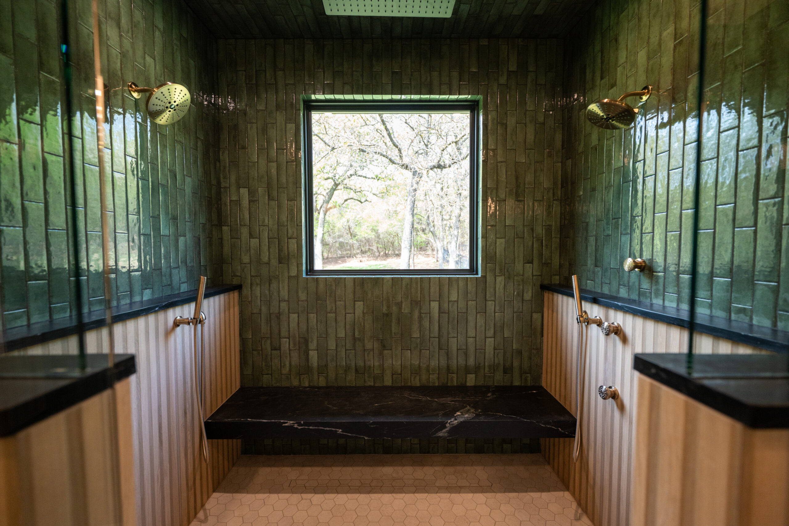 Walk-in shower with green tile walls, dual showerheads and black stone bench.
