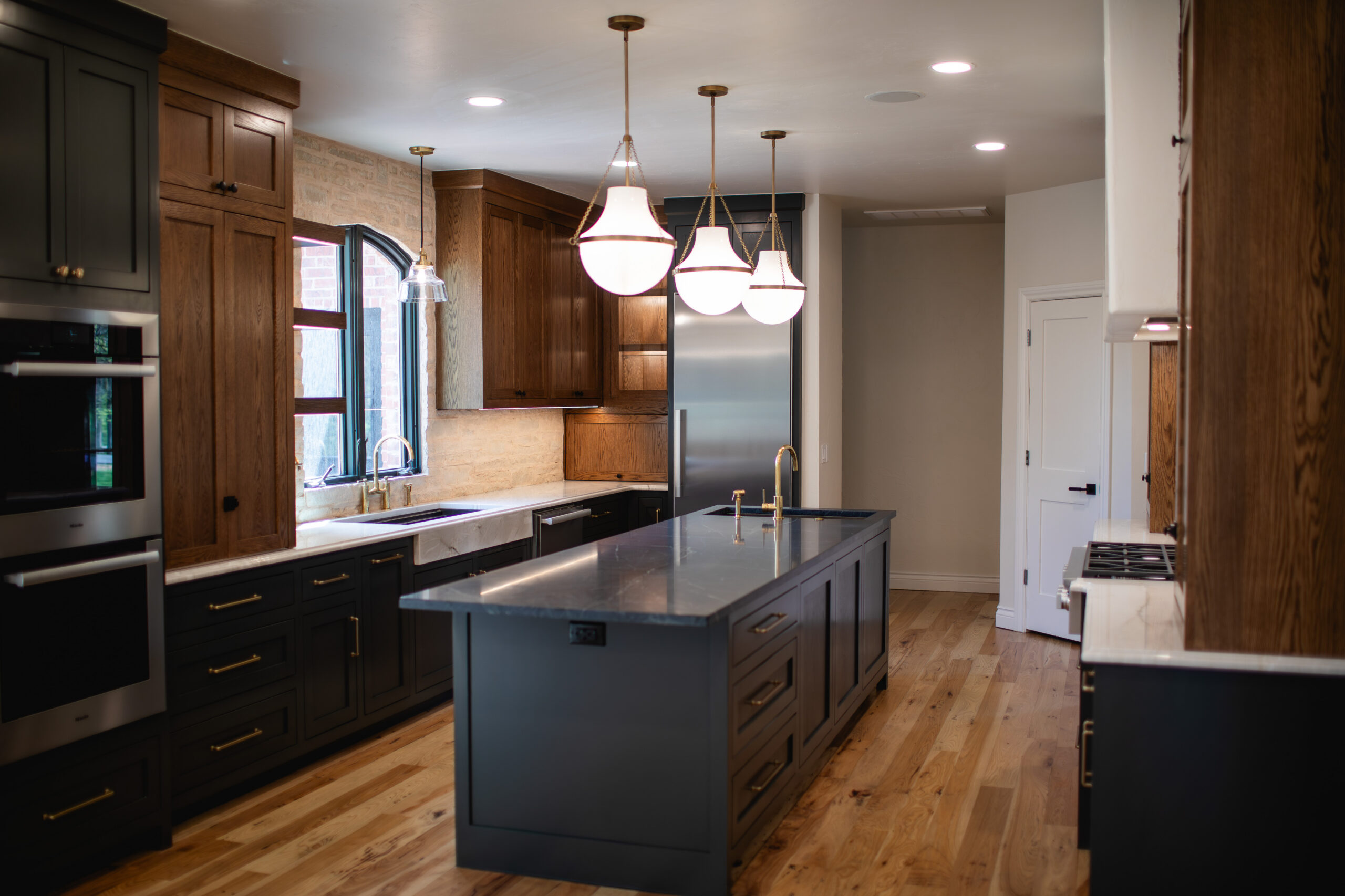 Spacious kitchen with dark island, wood cabinetry and pendant lighting.
